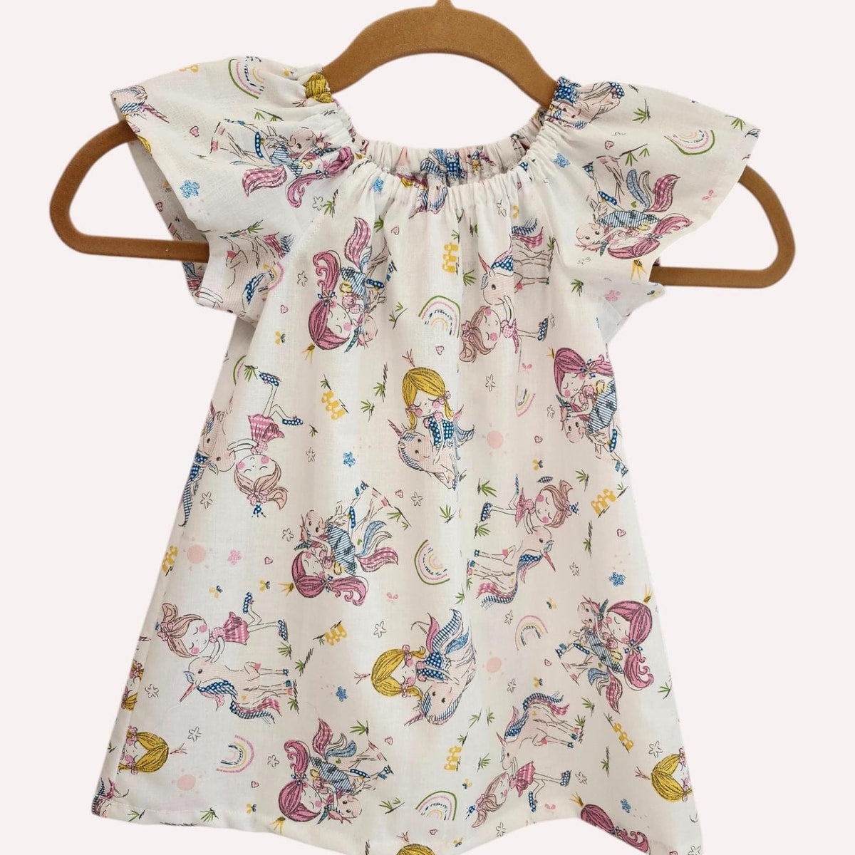 Children's dress with unicorn pattern on a hanger against a white background