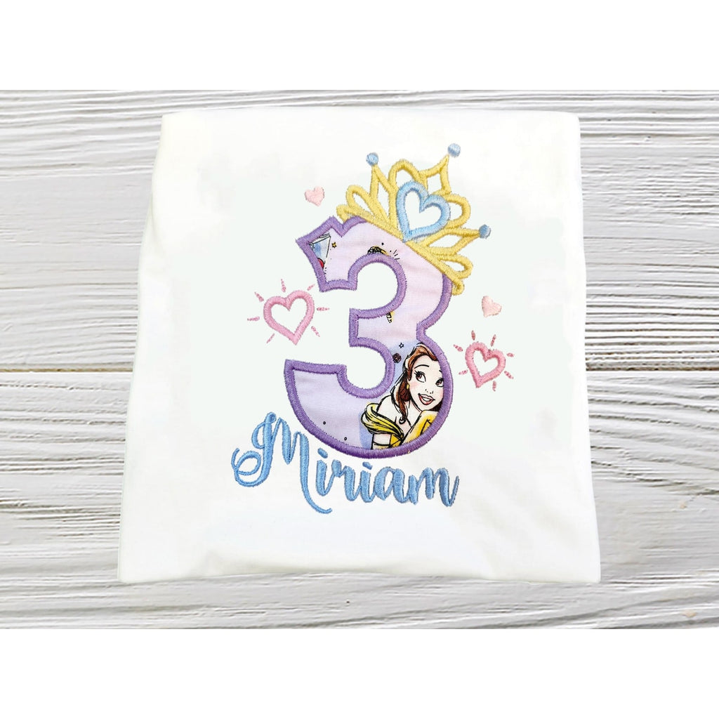 Children's shirt with number 3 and princess design on a wooden surface
