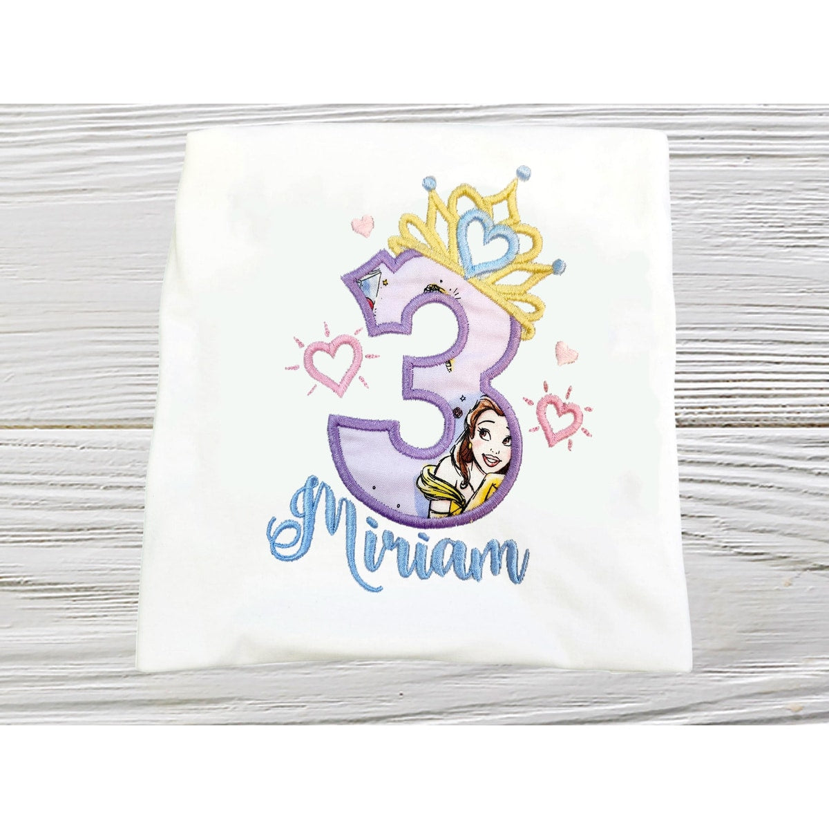 Children's shirt with number 3 and princess design on a wooden surface