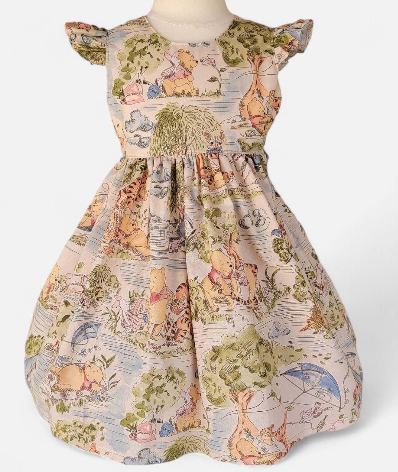Children's dress with Winnie the Pooh pattern on a mannequin against a white background