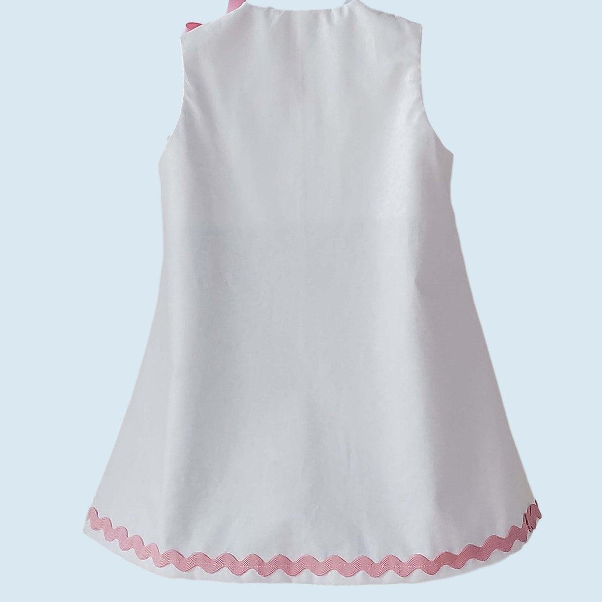 White sleeveless dress with pink trim on a light blue background