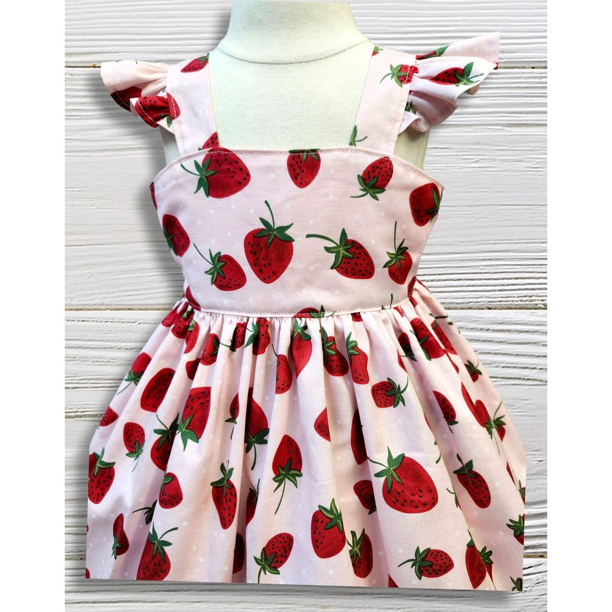 Children's dress with strawberry pattern on a mannequin against a white background