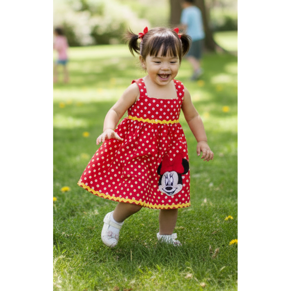 Child wearing a red polka dot dress with a cartoon character, standing on grass.