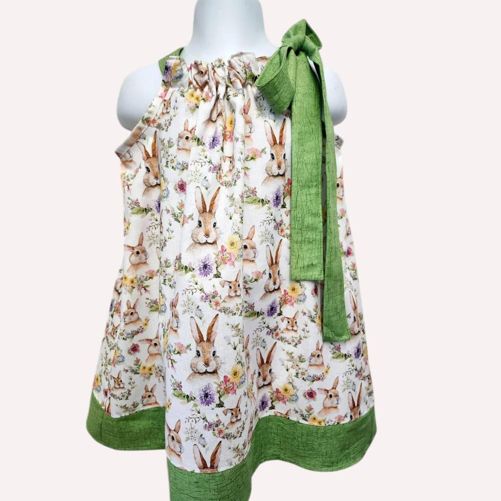 Children's dress with rabbit print and green trim on a mannequin against a white background