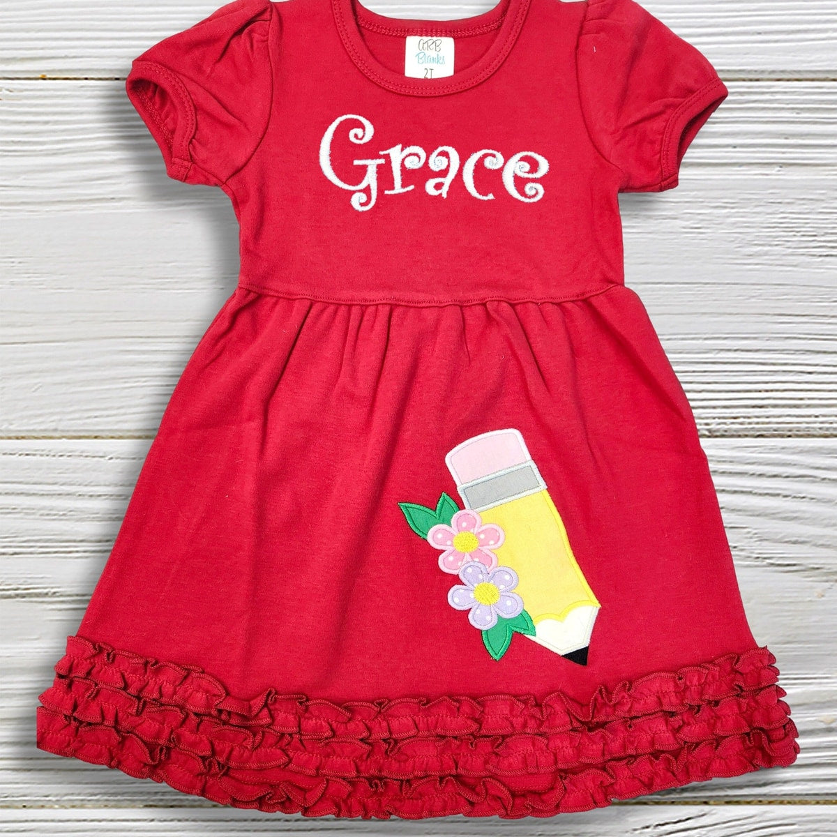 Red dress with 'Grace' printed on it and a pencil design on a wooden surface
