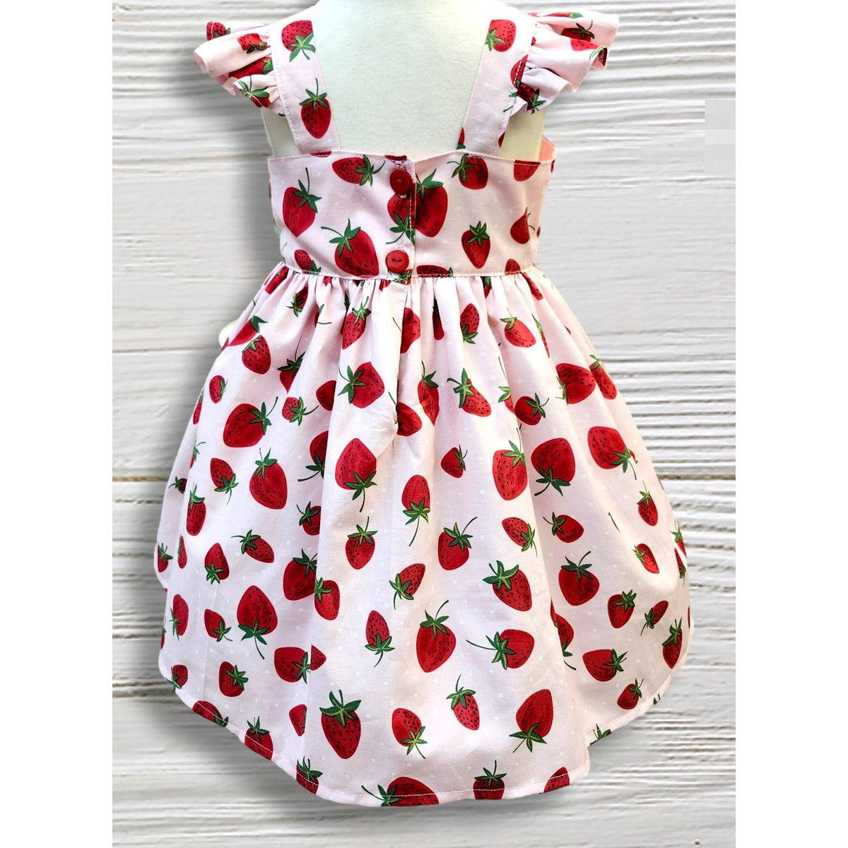 White dress with red strawberry pattern on a wooden surface