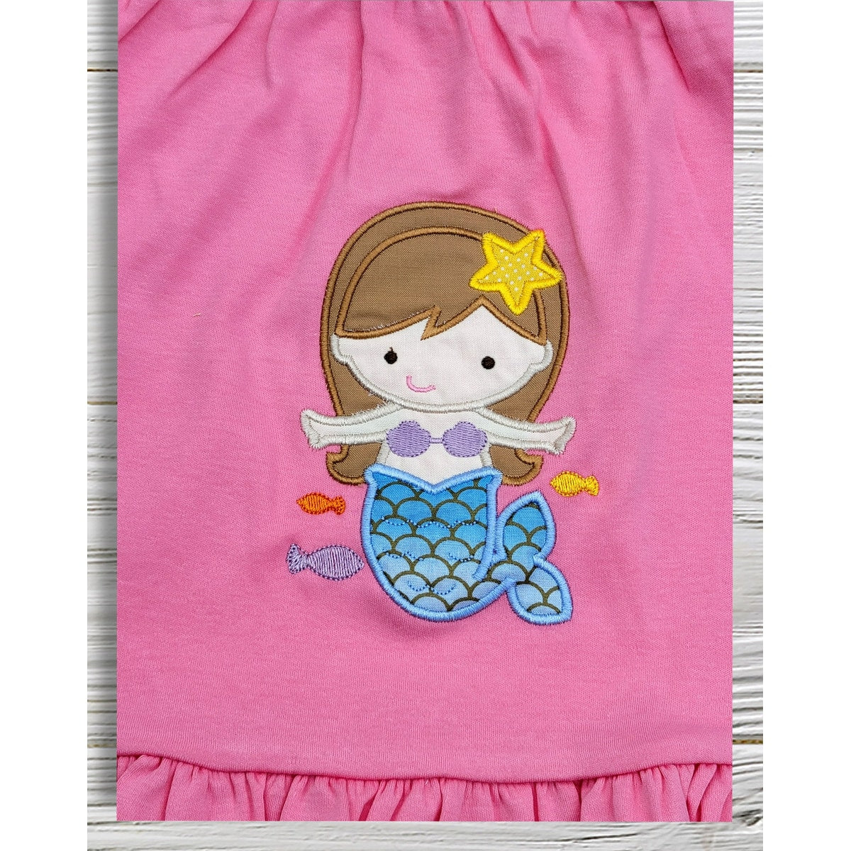Pink fabric with a mermaid applique on a wooden surface