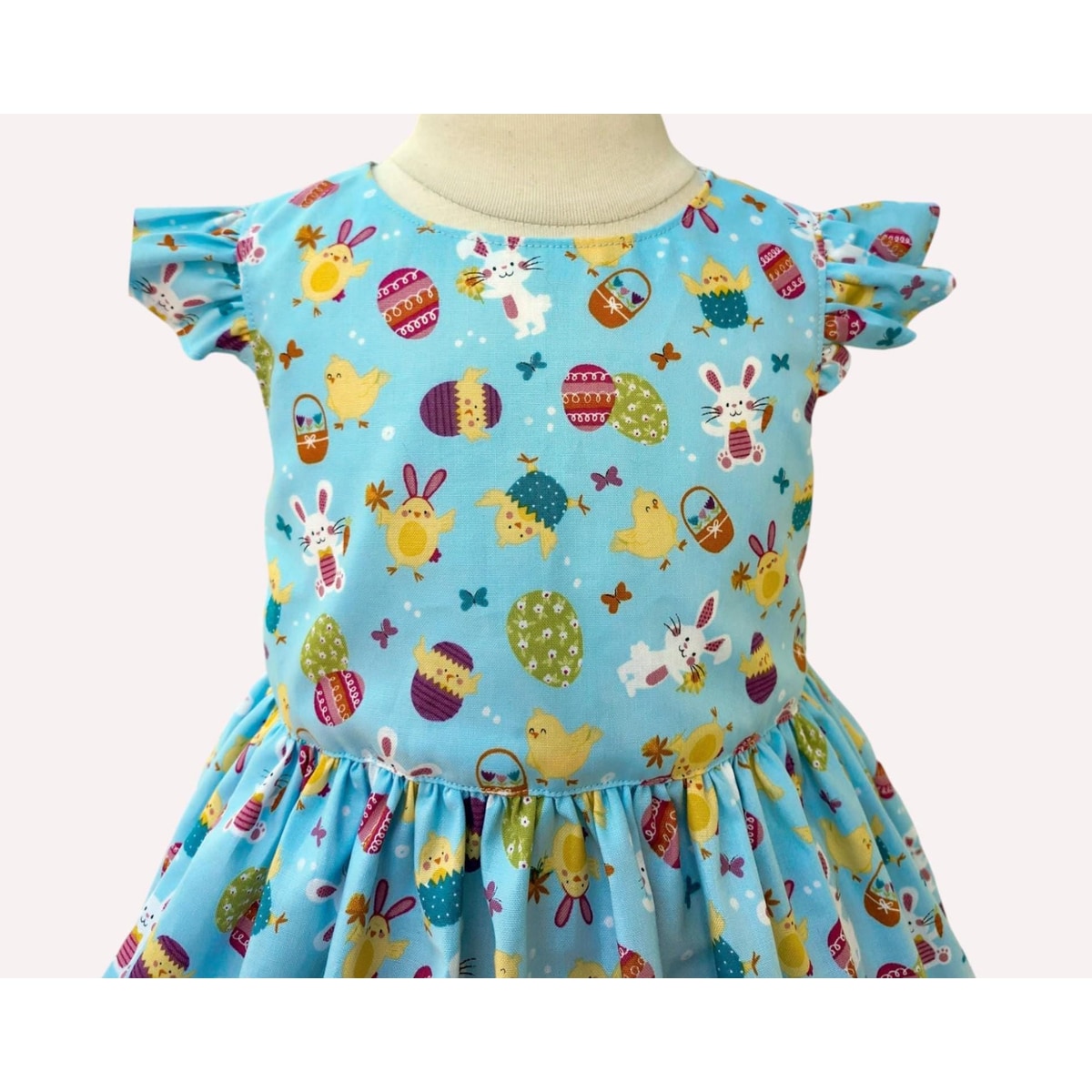 Children's dress with Easter-themed pattern on a mannequin against a white background