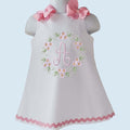 White dress with pink floral embroidery and bow accents on a light blue background