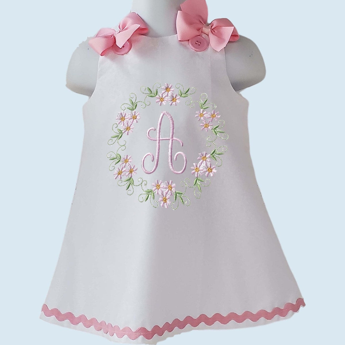 White dress with pink floral embroidery and bow accents on a light blue background