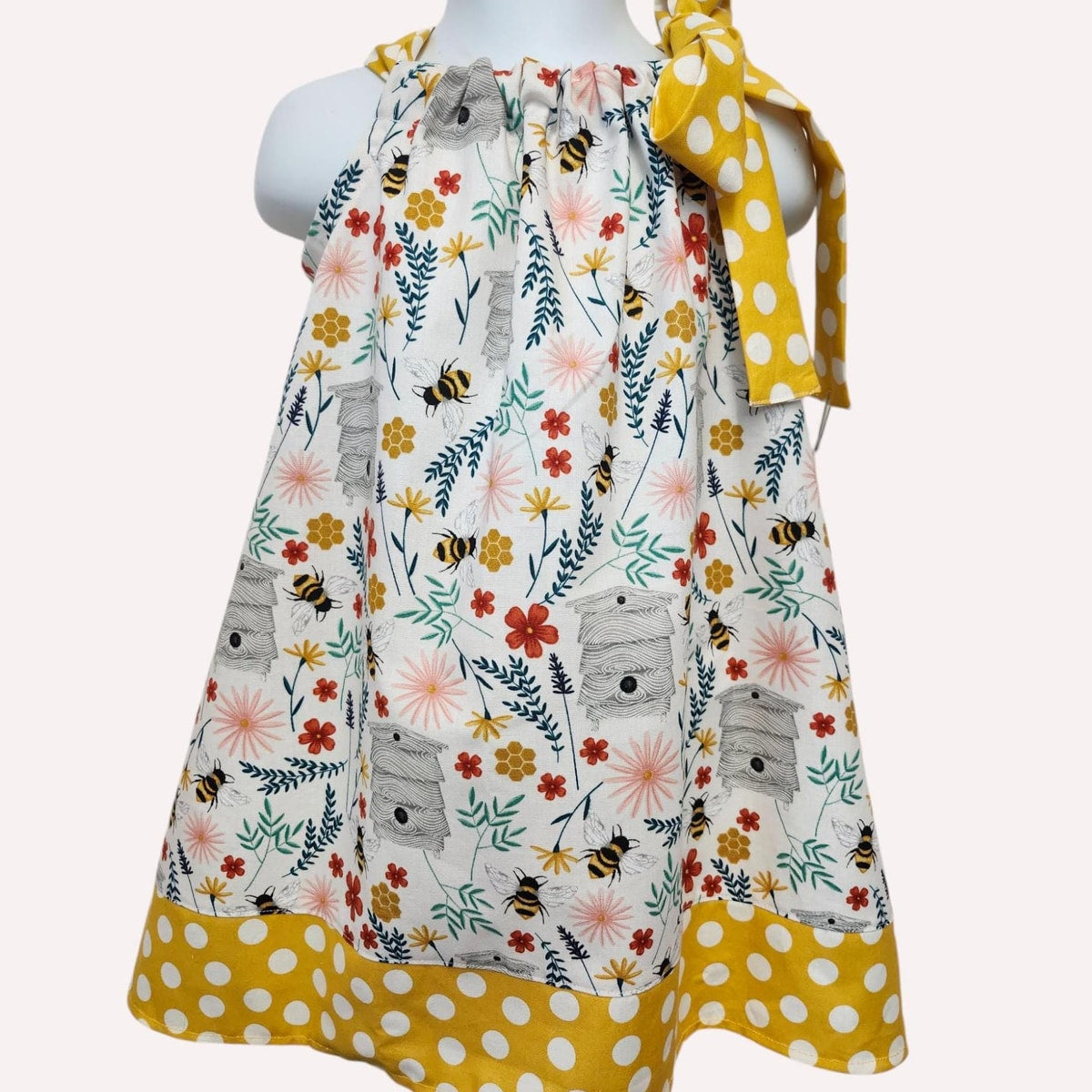 Children's dress with floral and bee pattern on a mannequin against a white background