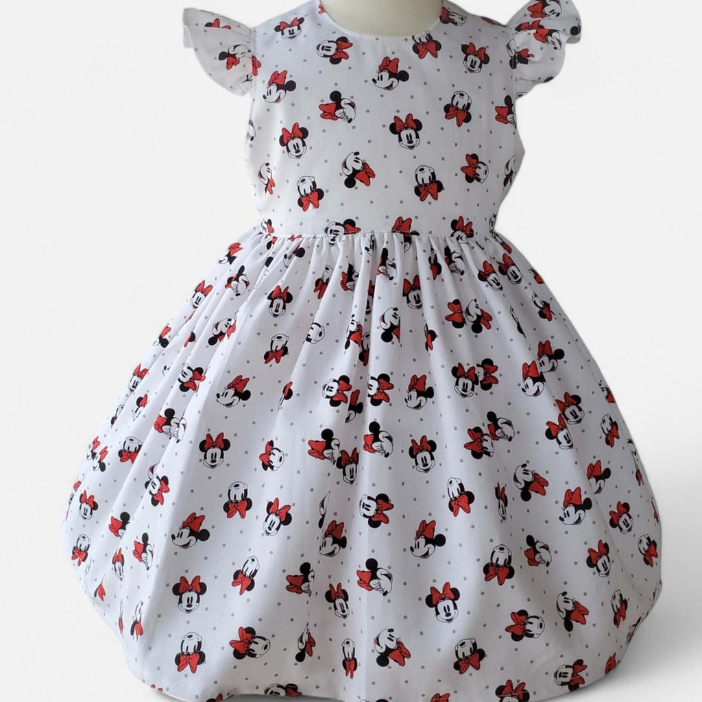Child in a floral dress standing in a park with flowers and trees in the background