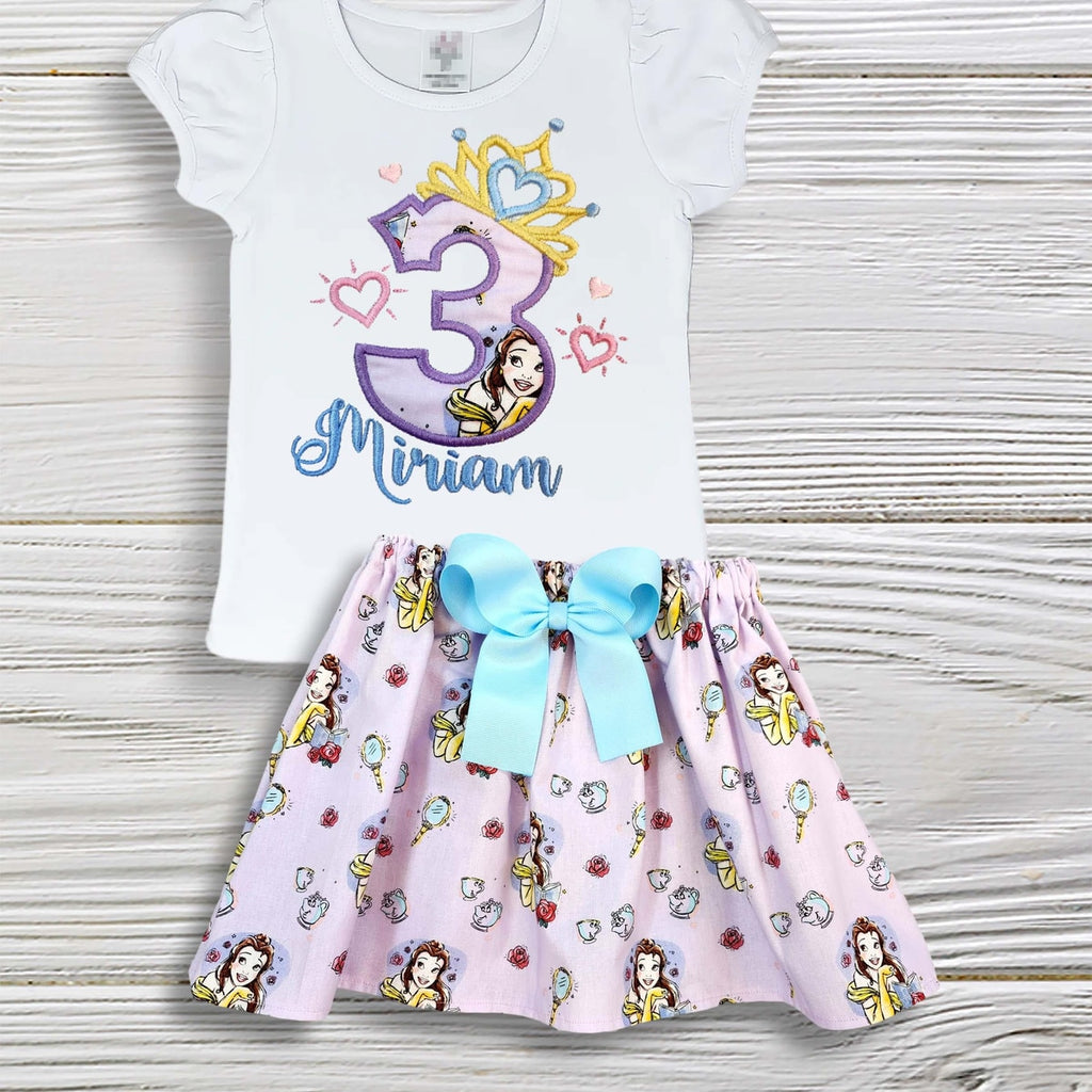 Children's outfit with a white top and pink skirt featuring Disney princesses on a wooden surface.