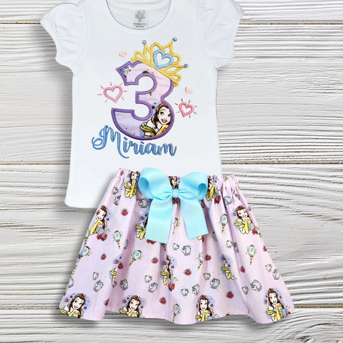 Children's outfit with a white top and pink skirt featuring Disney princesses on a wooden surface.