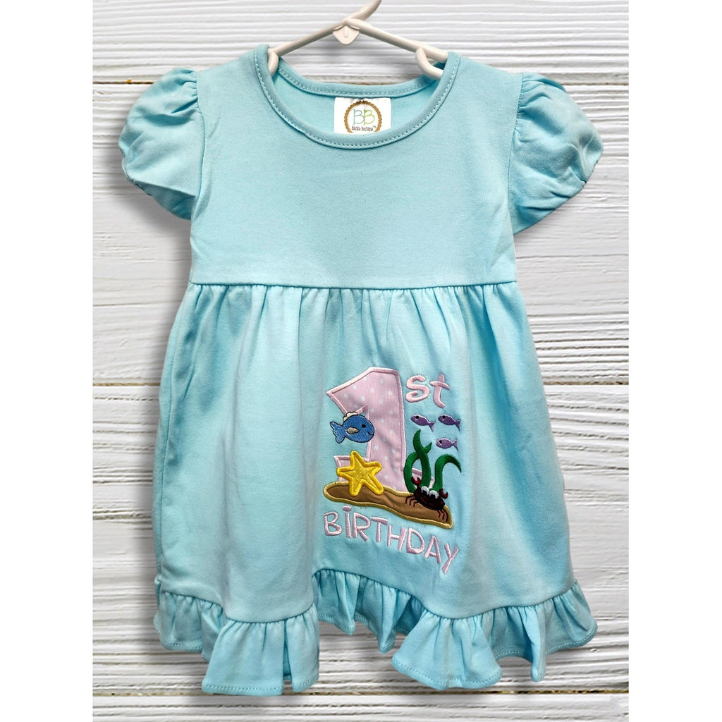 Light blue dress with '1st Birthday' and fish design on a wooden surface