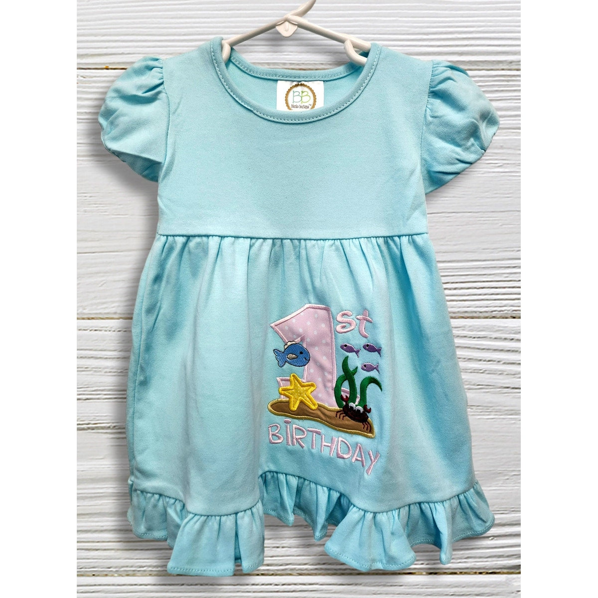 Light blue dress with '1st Birthday' and fish design on a wooden surface