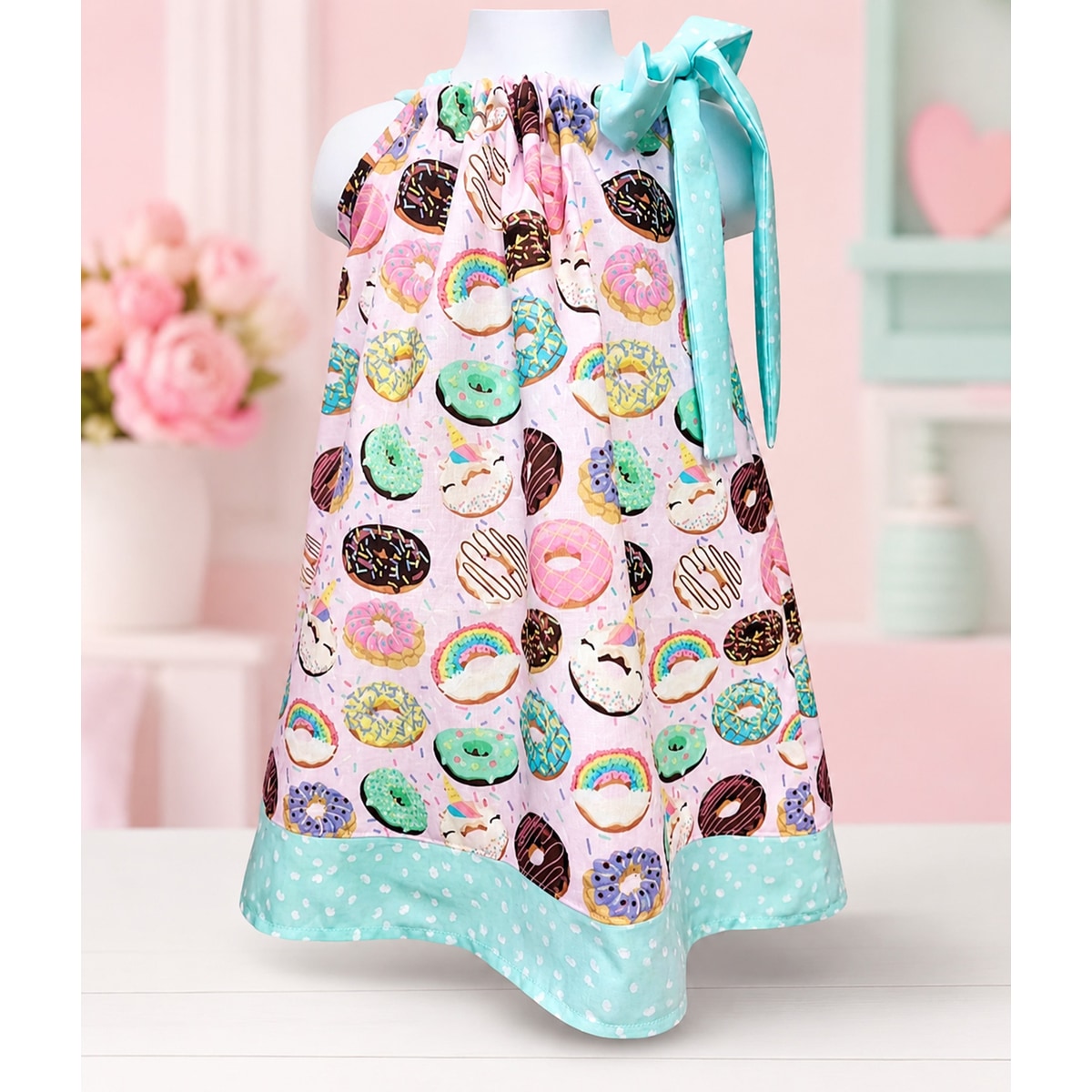 Colorful apron with donut pattern on a mannequin against a soft pink background