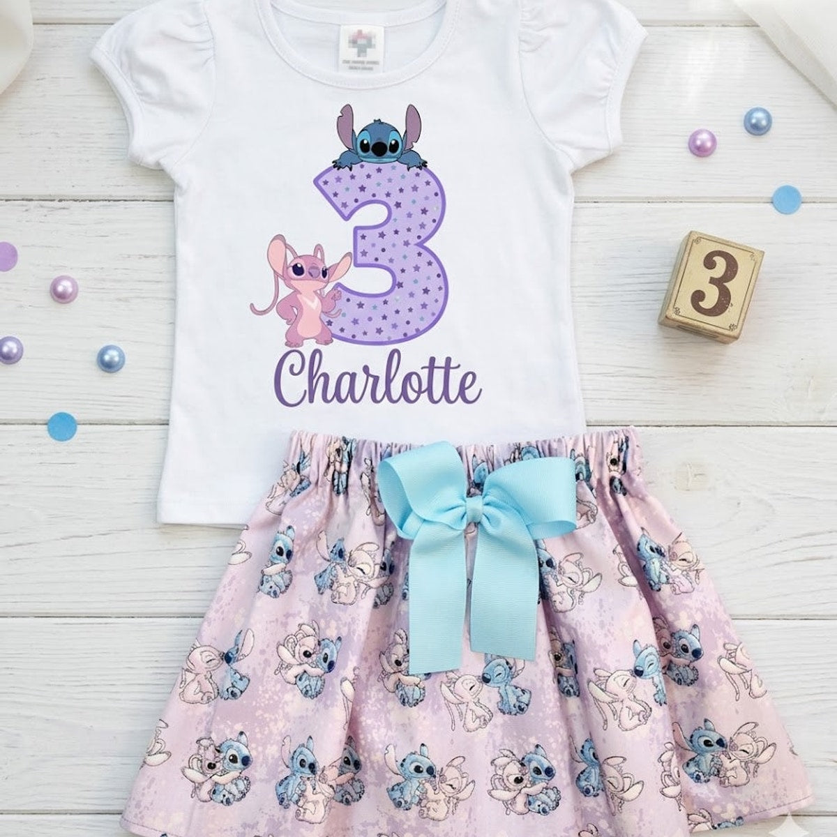 Children's outfit with white top and pink skirt featuring cartoon characters on a wooden surface.