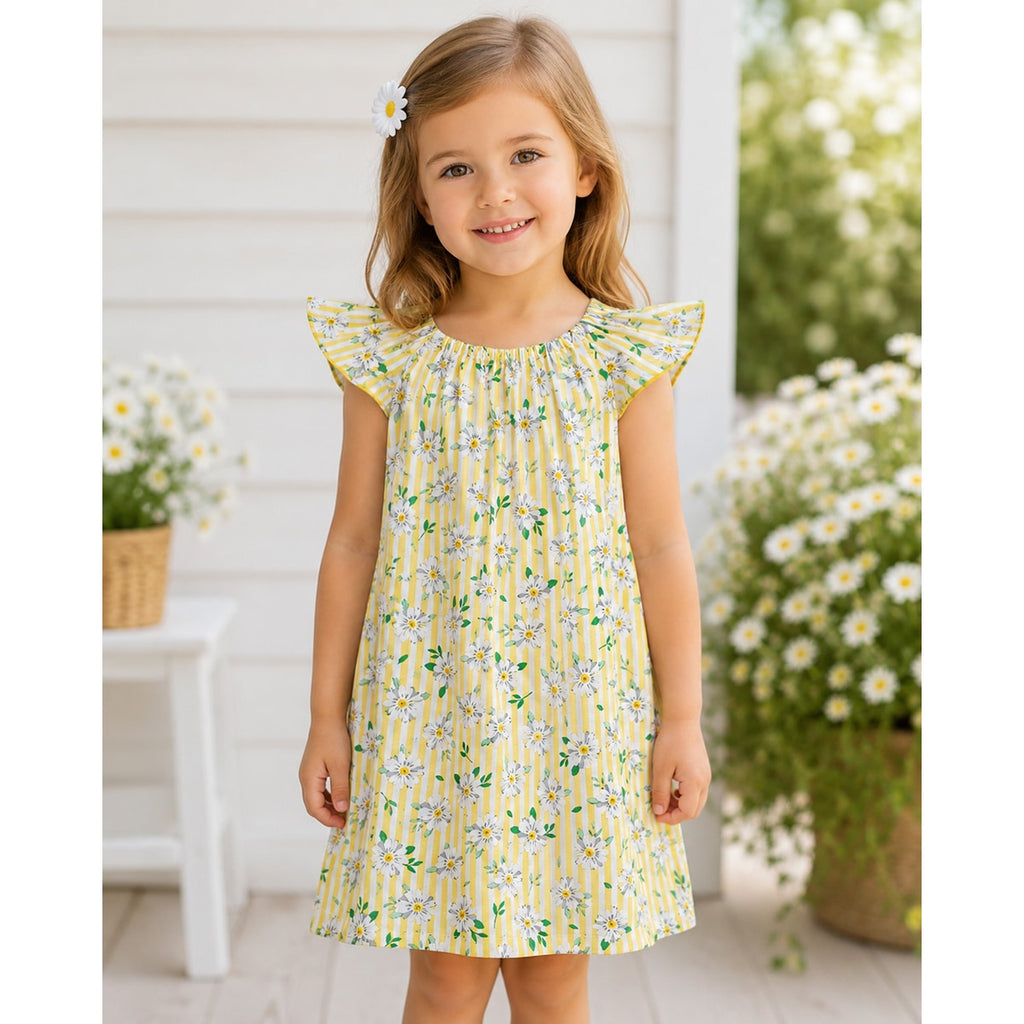 Young girl in a yellow floral dress standing outdoors with flowers in the background