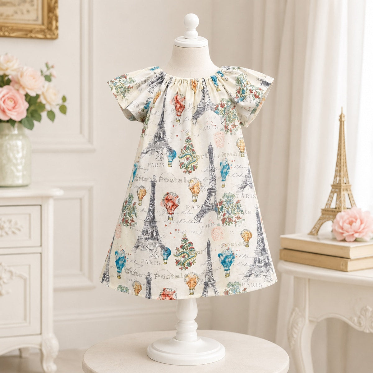 Children's dress with Eiffel Tower and hot air balloon print on a mannequin against a decorative background.