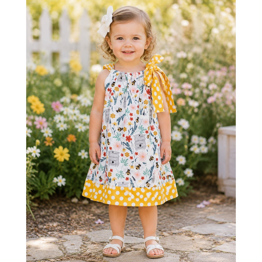 Young girl in a floral dress with yellow accents standing in a garden.