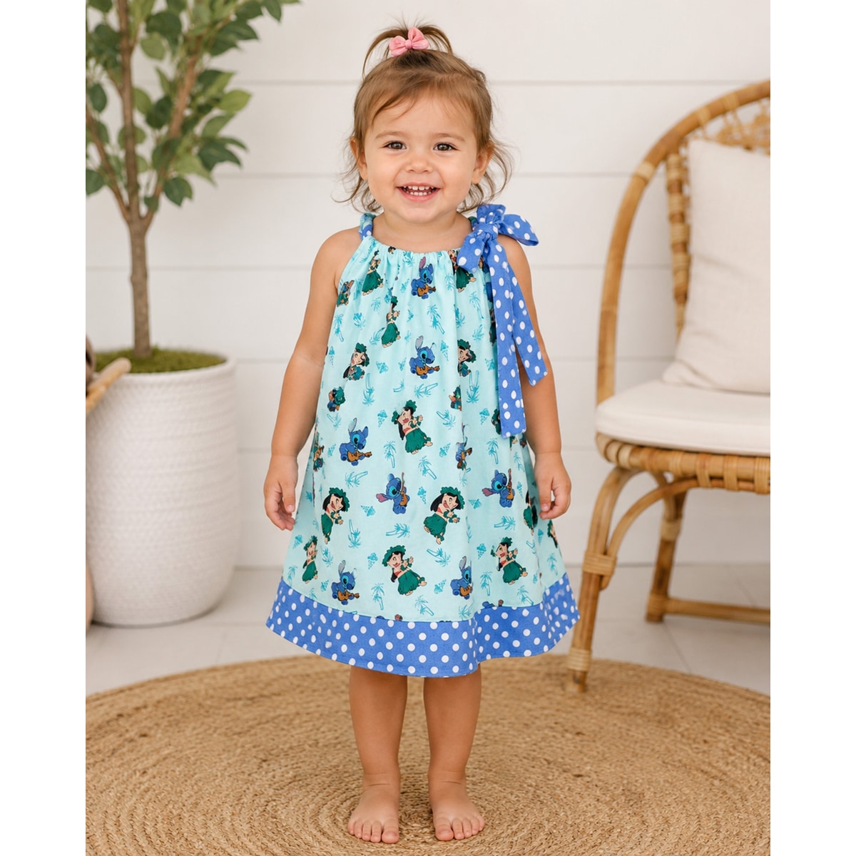 Child wearing a dress with cartoon characters and blue polka dot trim, standing on a woven mat.