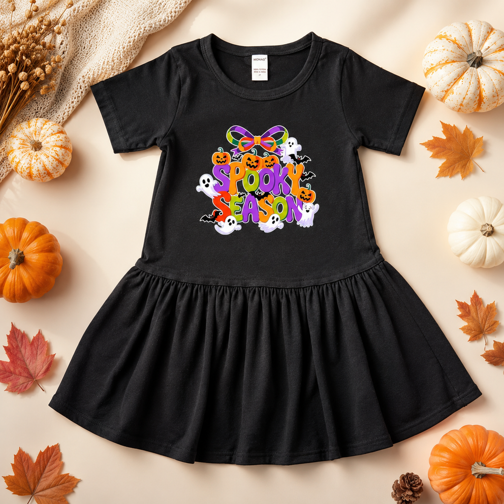 Black dress with 'Spooktacular Season' text on a beige background with pumpkins and leaves