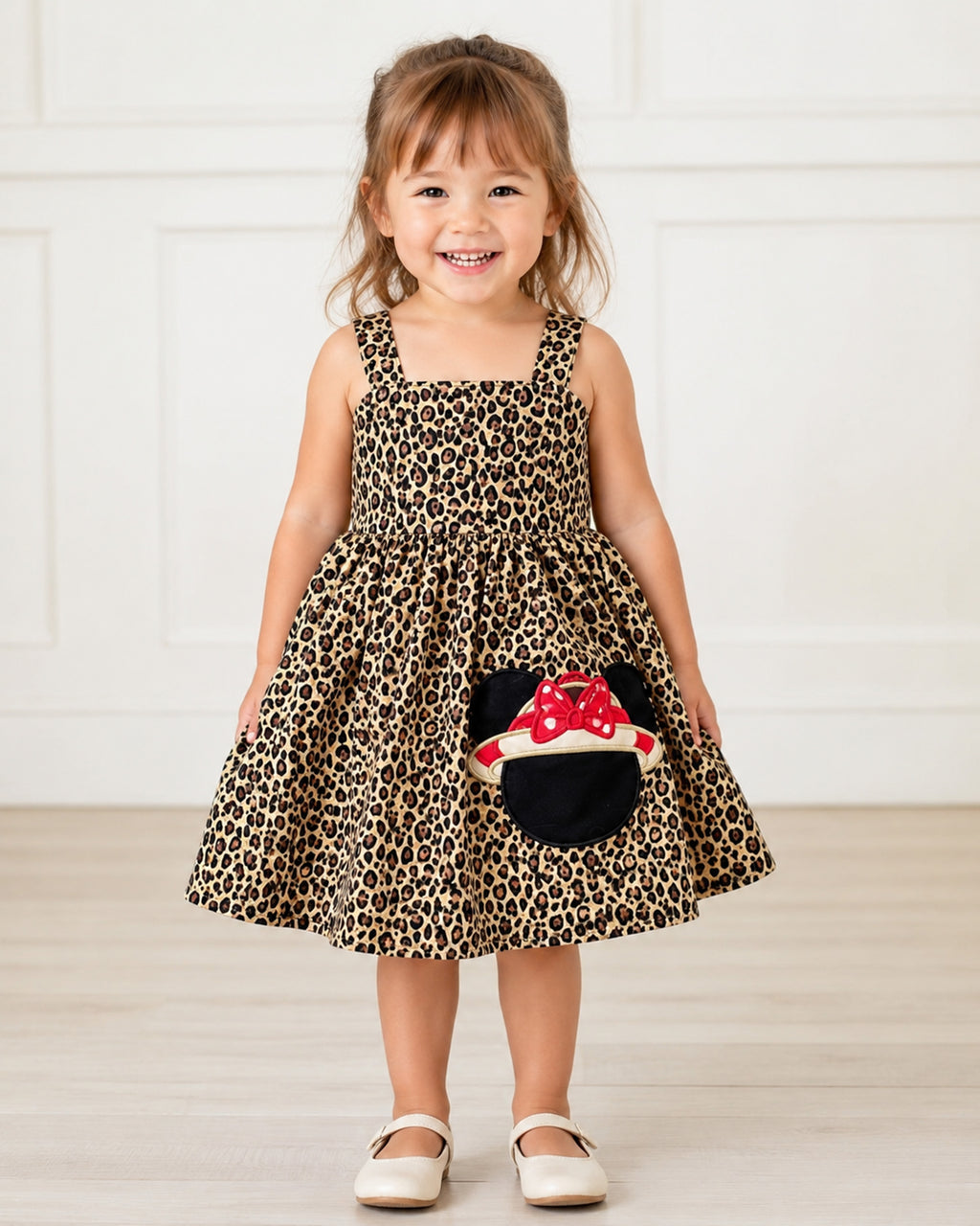 Child wearing a leopard print dress with a red and white character design, standing against a white background.