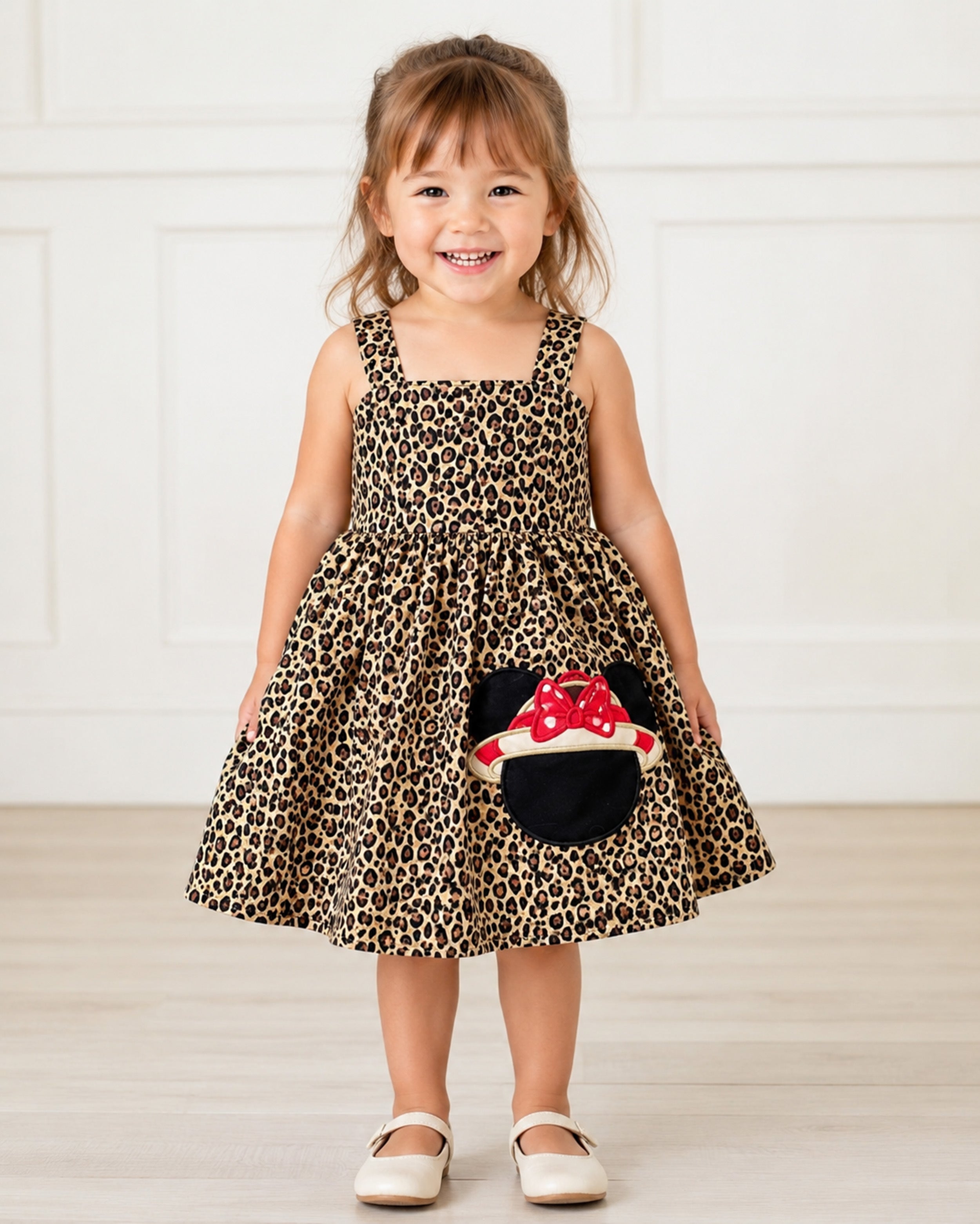 Child wearing a leopard print dress with a red and white character design, standing against a white background.