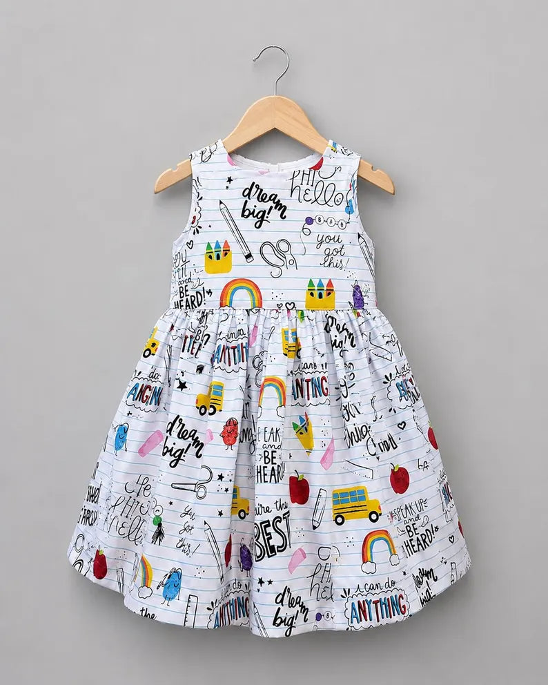A sleeveless white children's dress with a colorful school-themed print, hanging on a wooden hanger against a solid gray background.
