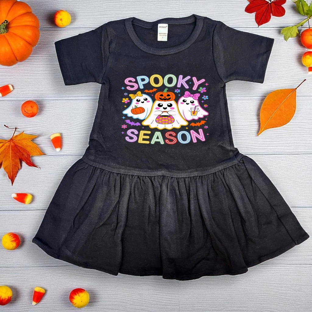 Black dress with Halloween-themed design on a wooden surface with fall decorations.