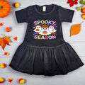 Black dress with Halloween-themed design on a wooden surface with fall decorations.