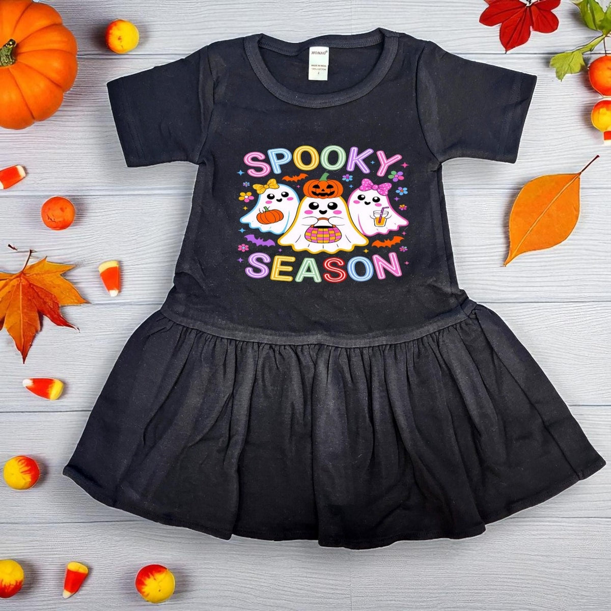 Black dress with Halloween-themed design on a wooden surface with fall decorations.