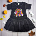 Black dress with Halloween-themed design on a wooden surface with pumpkins and leaves.