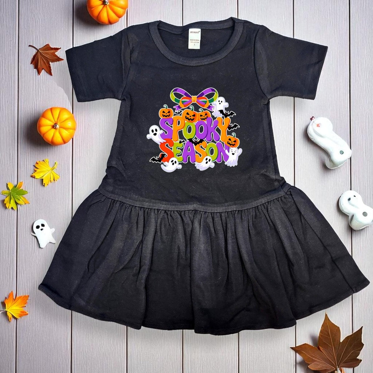 Black dress with Halloween-themed design on a wooden surface with pumpkins and leaves.