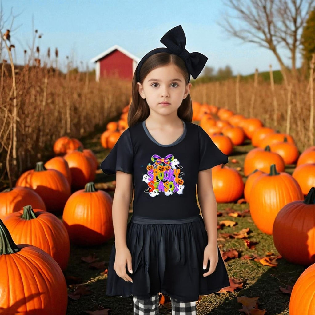Young girl in a black shirt with colorful design standing in a pumpkin patch.