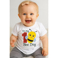 Baby wearing a white onesie with a bee design and text, sitting on a light-colored surface.
