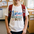 Child wearing a '1st grader reporting for duty' shirt with a red backpack in a classroom setting.
