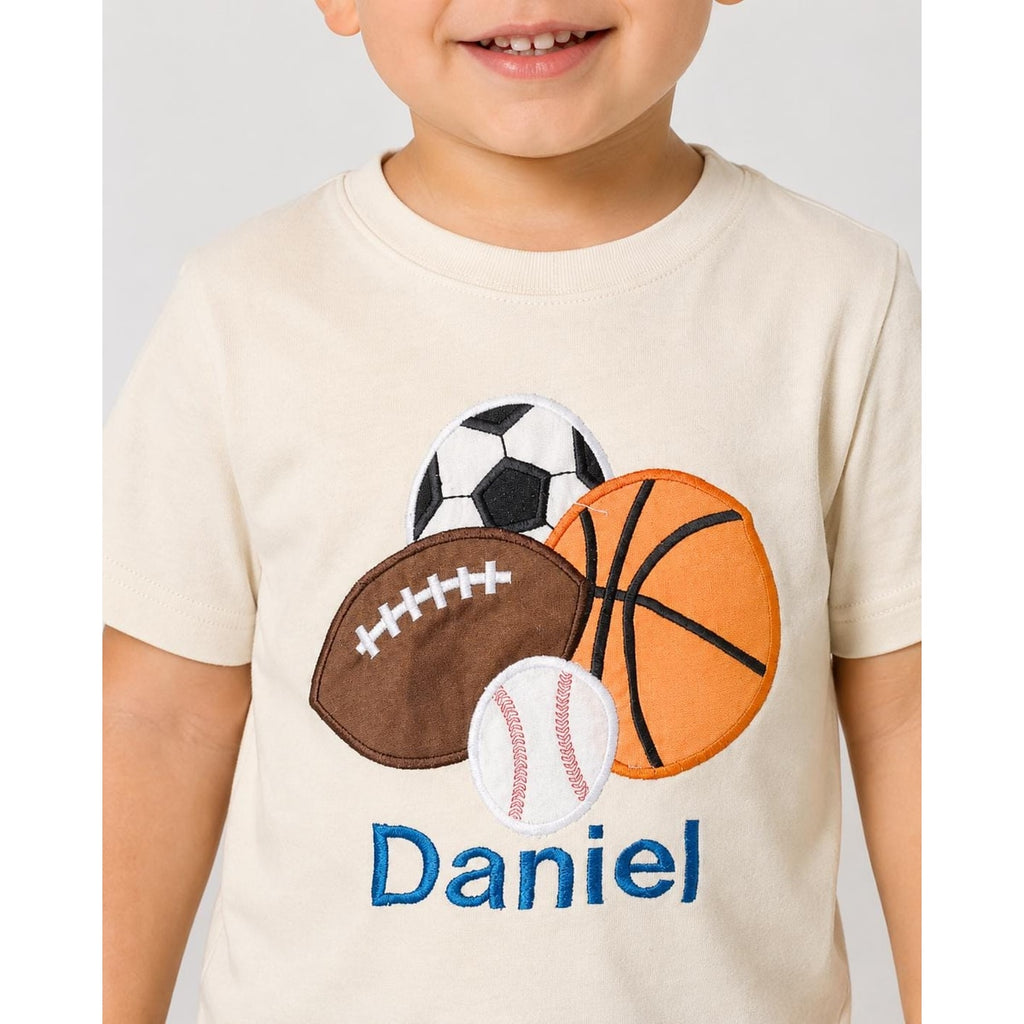 Child wearing a cream t-shirt with sports-themed appliqués and the name 'Daniel' on a plain background