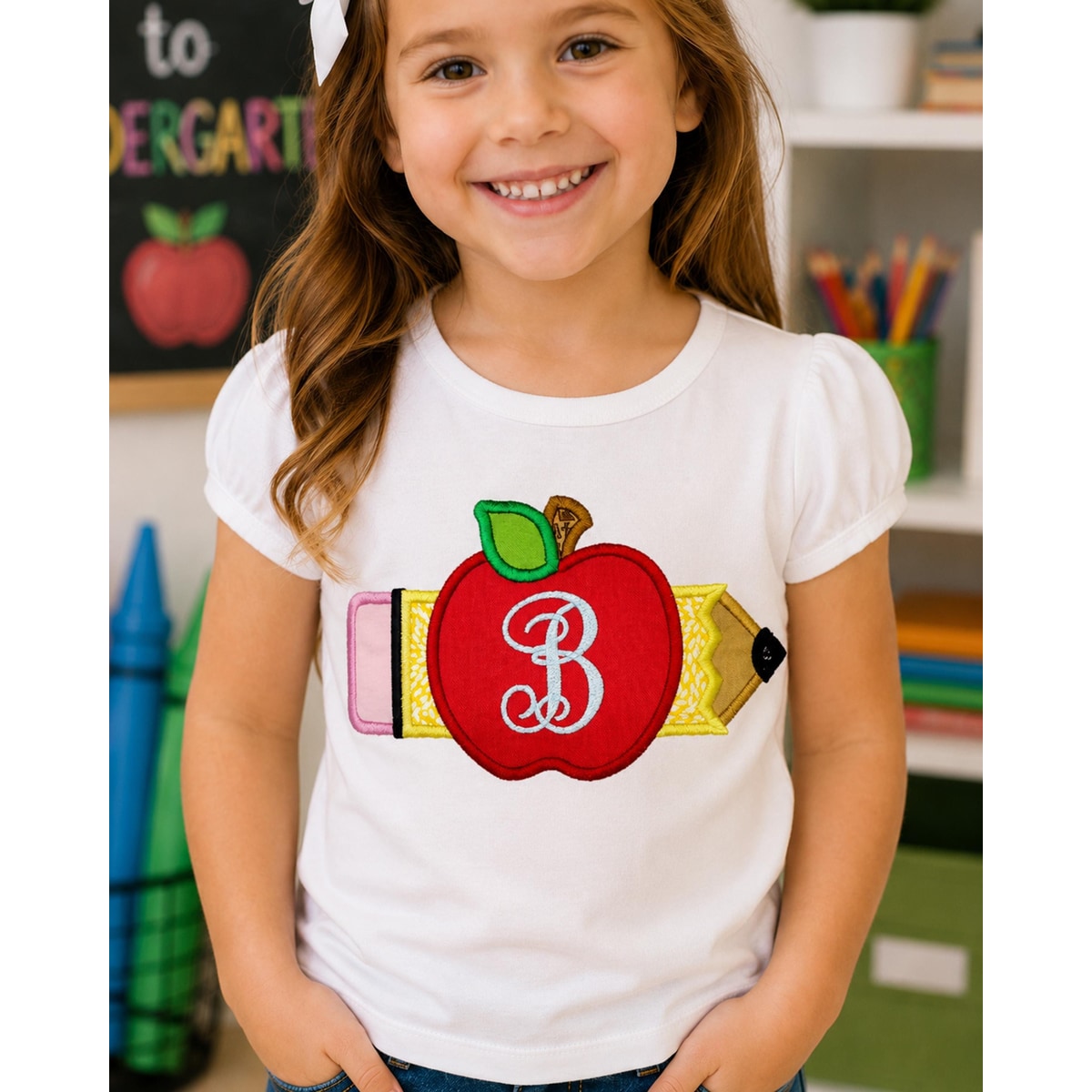 Young girl wearing a white t-shirt with an apple and pencil design, standing in a classroom setting.