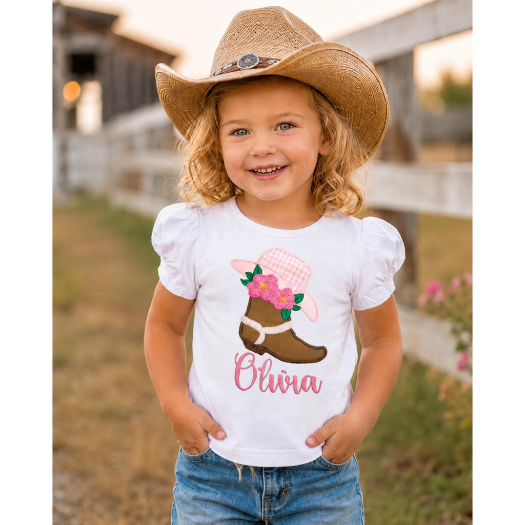 Child wearing a white shirt with a cowboy boot design and 'Olivia' text, standing outdoors.