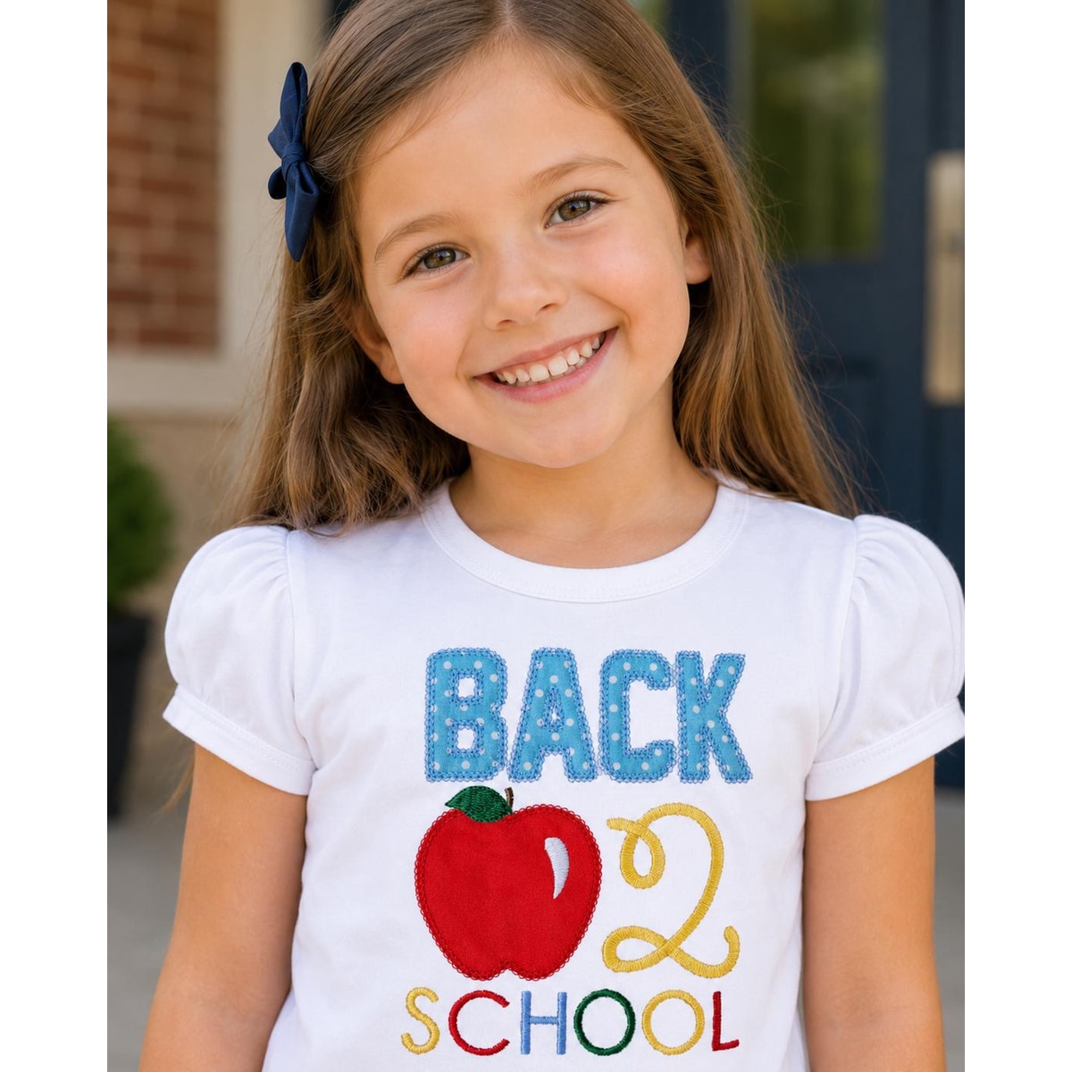 Young girl wearing a 'Back to School' shirt with an apple graphic.